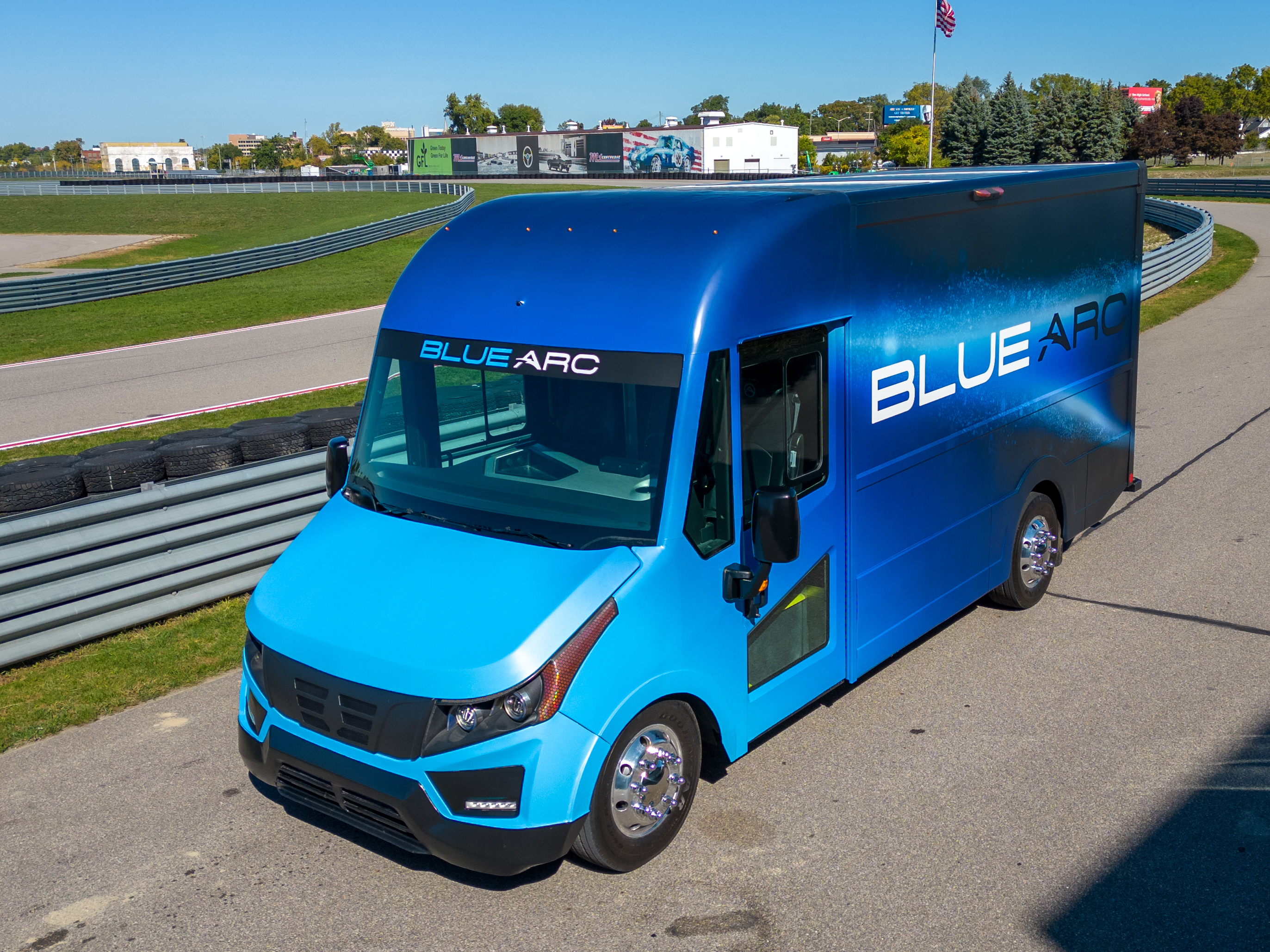 A blue electric delivery truck driving on a private road
